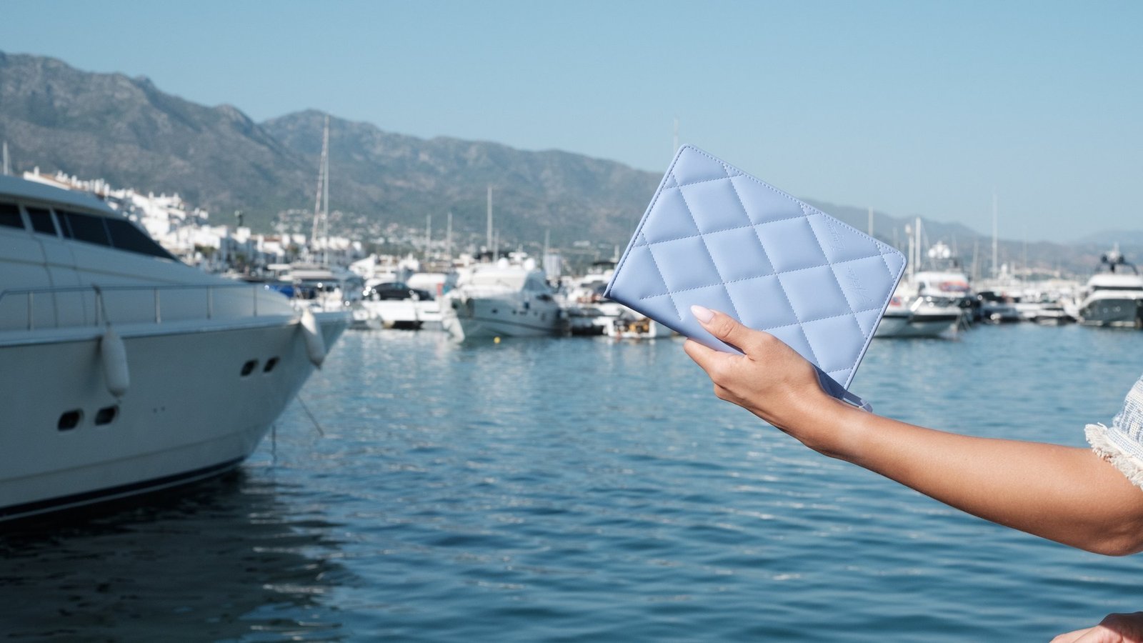 A quilted notebook held above the water in a Mediterranean marina